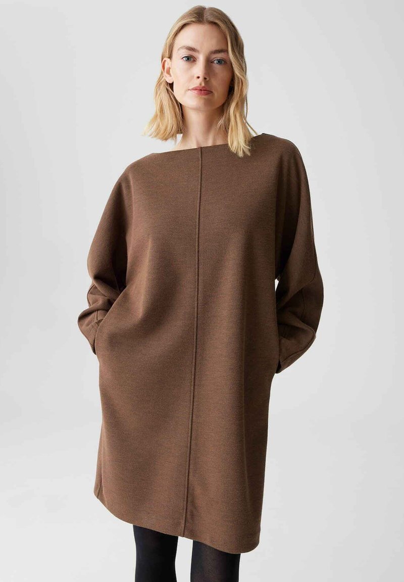 Bruine oversized jurk met een ronde halslijn, lange mouwen en een centrale naaddetail, gemaakt van een zachte, gestructureerde stof.