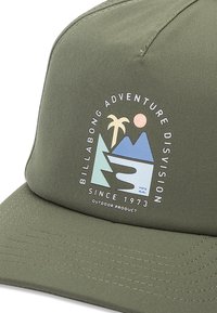 Olive green cap with a flat brim, featuring a printed graphic of mountains, a palm tree, and a sun in pastel colors. Stitching details visible.