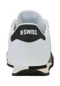 Bílé sportovní boty s černým akcentem na patě, na kterých je logo "K-Swiss". Texturovaná černá podrážka se bílými a černými pruhy po straně.