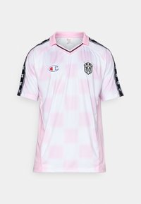 Lichtroze en witte voetbalshirt met een v-hals, zwarte schouderstrepen en een logo op de borst. Gemaakt van ademend materiaal.