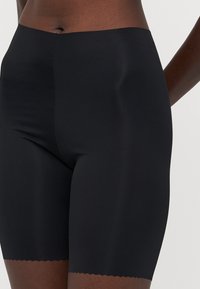 Høytlivede svarte shaping-shorts laget av glatt, elastisk materiale med en strukturert scalloped kant nederst.