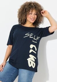 Camiseta de color azul marino de corte holgado con mangas cortas. Presenta el texto gráfico en blanco "SELF LOVE CLUB" en diferentes estilos en el frontal. Tejido suave.