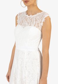Robe en dentelle blanche avec un motif floral, un col montant à bords festonnés, des manches courtes et une taille cintrée avec un bandeau lisse.