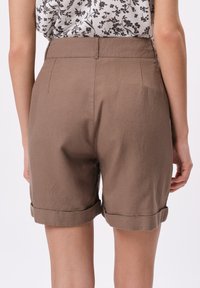 Brązowe lniane szorty z podwiniętym dołem, charakteryzujące się gładką teksturą i dopasowanym krojem, prezentowane z tyłu o prostym wzorze.