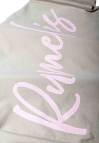 Beżowa tkanina z dużym, kursywnym różowym napisem "Romesh" nadrukowanym na całej powierzchni.