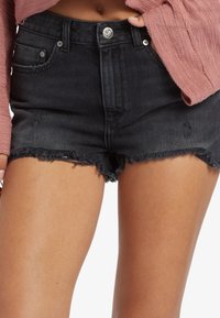 Bermudas de mezclilla negras con un dobladillo deshilachado, detalles desgastados y un diseño ajustado. Presenta herrajes de metal y un cierre de botón.