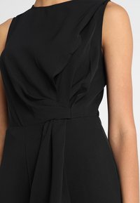 Czarna sukienka z drapowanym topem, bezrękawowym designem i związanym w pasie detalem. Gładki materiał o miękkiej teksturze i prostych liniach.