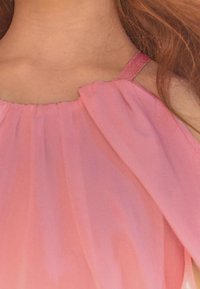 Ljusrosa ärmlös topp med en volangkrage och tunna axelband, tillverkad av ett mjukt, flödande tyg som faller mjukt.