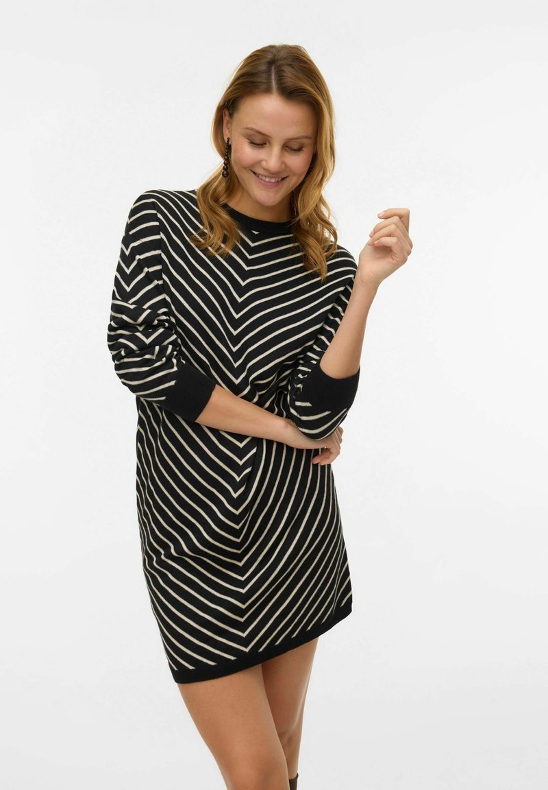 Juoda ir kreminė su juostelėmis suknelė laisvo silueto, ilgomis rankovėmis ir apvaliu iškirptės kraštu, puošta zigzago raštu ir ribotais rankogaliais.