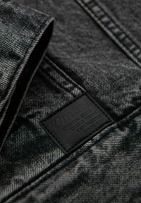 Tessuto denim in tonalità di nero e grigio; presenta una superficie testurizzata e un'etichetta in pelle nera con testo in rilievo.
