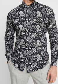 Camicia nera con motivo paisley bianco, colletto button-down e maniche lunghe, realizzata in un tessuto morbido con una vestibilità slim.