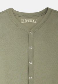 Camicia in cotone a coste verde oliva con scollatura a V e bottoni a pressione argentati sul davanti. I dettagli dell'etichetta sono visibili all'interno del colletto.