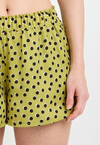 Shorts verts avec des pois noirs et blancs, dotés d'une taille élastique et d'un tissu lisse. Le design comprend une coupe décontractée et des coutures latérales.