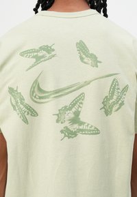 Light green T-shirt featuring a large green Nike logo surrounded by butterfly graphics on the back. Soft cotton texture.