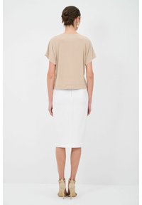 Krémový top s krátkým rukávem v kombinaci s bílou tužkovou sukní a béžovými stiletto podpatky. Hladké látky, přiléhavý střih a minimalistický design.