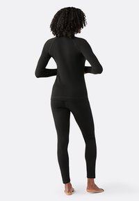 Musta pitkähihaisen rash guard, jossa on slim fit ja raglan-hihat, yhdistettynä tiukkoihin mustiin legginsseihin; molemmat ovat venyviä ja niissä on sileä pinta.