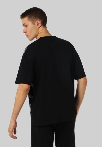 T-shirt in cotone nero con vestibilità rilassata, maniche corte, design sul retro con elementi grafici leggeri, colletto tondo e una texture liscia.