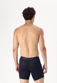 Marineblaue Boxer-Briefs aus weichem Stoff, mit einem breiten elastischen Bund, die eng anliegen und eine mittellange Oberschenkel-Länge sowie minimale Details aufweisen.