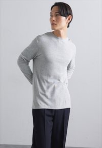Graumeliertes Langarm-T-Shirt aus weichem Material, mit Rundhalsausschnitt und taillierter Passform. Kombiniert mit dunklen Hosen, sorgt für einen einfachen, sauberen Look.