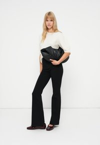 Black flared pants, cream knit top, and glossy burgundy shoes. Holding a large black leather bag with a smooth texture, minimal detailing.