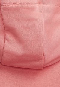 Rosa sweatshirttyg med en mjuk textur, som har en huva och synliga sömmar. Materialet verkar mjukt och stretcht.