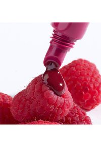 Lampone con un liquido rosso scuro e lucido che sgocciola da un tubo magenta. La superficie è texturizzata, enfatizzando i peli sottili e le fossette del lampone.
