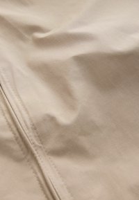 Világosbézs színű, sima textúrájú szövet, enyhe gyűrődésekkel és jól látható varrással. Az anyag könnyűnek és tartósnak tűnik.