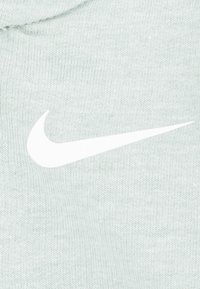 Ύφασμα φούτερ σε ανοιχτό πράσινο με απαλή υφή, με μεγάλο λευκό λογότυπο Nike swoosh στο κέντρο.