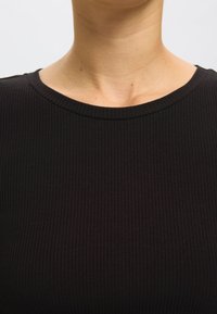 Must mustriga kampsun, millel on ümar kaelus ja sile tekstuur. Muster koosneb kitsastest vertikaalsetest ribadest.