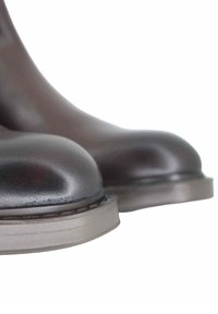 Stivaletti alla caviglia in pelle marrone con texture liscia, punta arrotondata e suola in gomma chiara. Focus sui dettagli del materiale superiore.