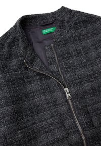 Czarna teksturowana kurtka z przednim zamkiem błyskawicznym, z okrągłym kołnierzem i subtelnymi detalami szwów. Podszewka wewnętrzna z widoczną metką marki.