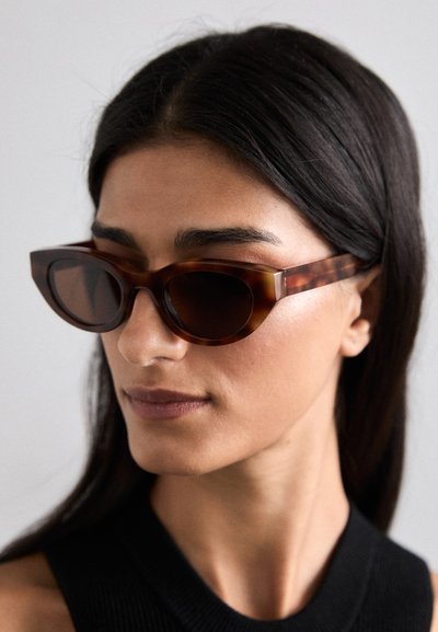 Ochelari de soare din material tartan cu formă geometrică în stil cat-eye, cu lentile întunecate și ramă groasă din acetat lucios. Prezintă detalii fine de marmorat.