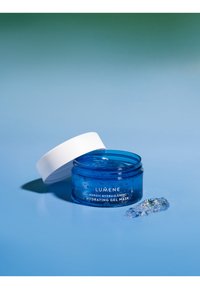 Pot bleu de masque hydratant Lumene avec un couvercle à vis blanc, rempli d'un produit clair et gélatineux, avec un morceau de gel à proximité.