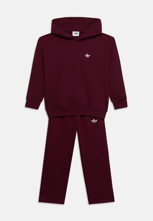 Mørk bordeaux hoodie og bukser sæt med hvide Adidas trefoil logoer på brystet og venstre lår, vist på ensfarvet baggrund.
