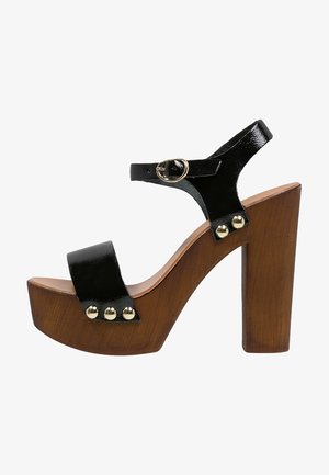 Sandalia de plataforma de charol negro con correa en el tobillo, hebilla dorada, tachuelas doradas y tacón alto grueso de madera.