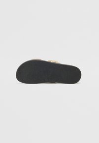 Svart gummisåle av en sandale med en teksturert overflate og en dekorativ stropp med en lys, metallisk glans.