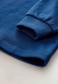 Camisa de algodón azul de manga larga con puños y dobladillo acanalados, con una textura suave y costuras planas. Sin patrones ni detalles adicionales.