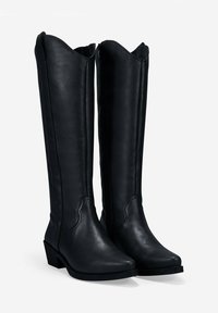 Botas de cuero negras hasta la rodilla con punta afilada, tacón bajo y borde superior con ondas. Textura suave y minimalismo en los adornos.
