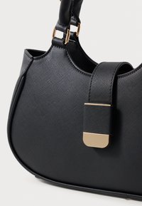 Bolso de mano negro con textura y forma curva, que presenta un accentuado en dorado y una correa acolchada para mayor comodidad.