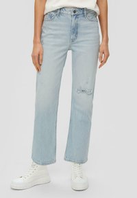 Jeans dritti strappati azzurro chiaro con vita alta e dettagli di scolorimento sottili. Abbinati a sneakers bianche con piattaforma.