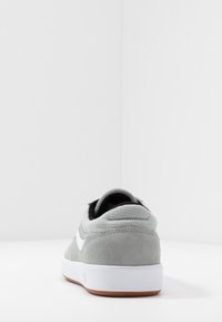 Baskets en daim gris avec accents blancs, semelle plate blanche, talon texturé. Avant lisse et col rembourré pour le confort. Design simple et classique.