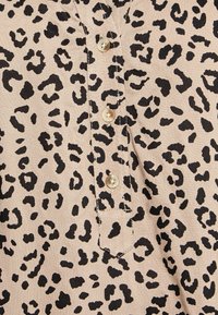 Leopardmönstrad tyg i beige med svarta fläckar. Har en knapplist med två runda knappar och en liten bröstficka.