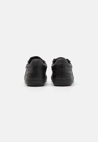 Sneakers neri in pelle con una texture liscia, caratterizzati da un design a scollo basso, suola piatta in gomma e dettagli di cucitura discreti sui lati.