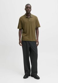 Olivgrön mönstrad poloskjorta med korta ärmar, i kombination med vida mörkgrå byxor och kraftiga svarta skor.