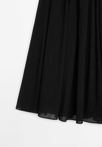 Jupe midi plissée noire en tissu léger semi-transparent avec une silhouette fluide sur fond blanc.