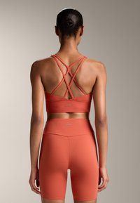 Piros sportmelltartó keresztbe fonott hátsó pántokkal és magas derekú, hozzá illő sortokkal; sima textúra és minimális márkázás a derekán.