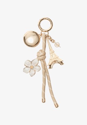 Nøglering med guldfarvet vedhæng, der indeholder en rund perle, en Eiffel-tårn vedhæng, en hvid blomst og en beige stofrem med båndmønster.