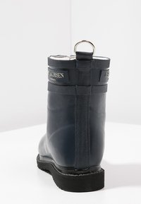 Bota de goma impermeable de color azul oscuro con un acabado texturizado, con una lengüeta en la parte superior y un forro blanco en contraste, que presenta un branding mínimo.