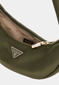 Borsa a spalla verde oliva realizzata in tessuto morbido. Presenta una cerniera oro e un'etichetta con logo triangolare. Interno foderato con motivo del nome del marchio.
