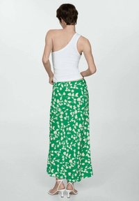 Maxi gonna floreale verde con un motivo floreale bianco, abbinata a un top senza spalline bianco e sandali con tacco bianchi.